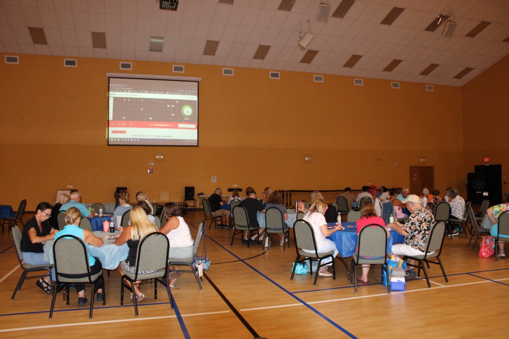 Two men sit at a check-in table with snacks and bingo materials in a gym